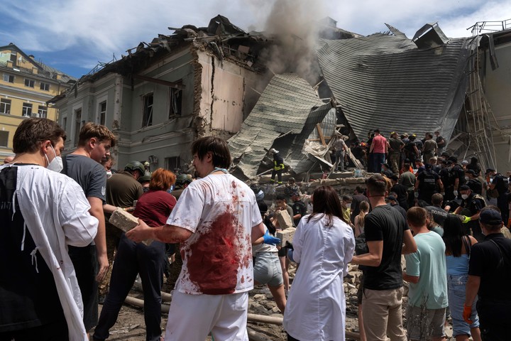 Rescatistas, voluntarios y trabajadores médicos, algunos con uniformes ensangrentados, limpian los escombros y buscan víctimas después de que un misil ruso impactara en el principal hospital infantil del país, Okhmadit, en Kiev. Foto AP