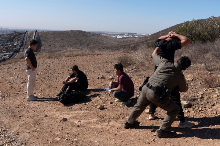 Un policía de frontera revisa a un grupo de migrantes que cruzaron desde México a Estados Unidos de forma ilegal, en San Diego, California. Foto: AP  