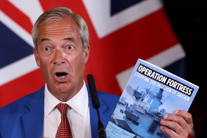 El líder del partido británico Reform UK, Nigel Farage, sostiene un folleto en el que se lee «Operación Fortaleza: Detener la invasión de Gran Bretaña» mientras habla durante una conferencia de prensa junto al portavoz de asuntos internos del partido, Zia Yusuf, en Londres, Gran Bretaña, el 3 de agosto de 2026. REUTERS/Toby Melville     
