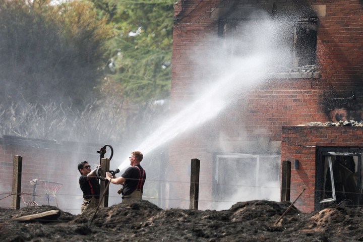 Bomberos apagan un incendio en una casa afectada por un fuego forestal. Foto: Reuters