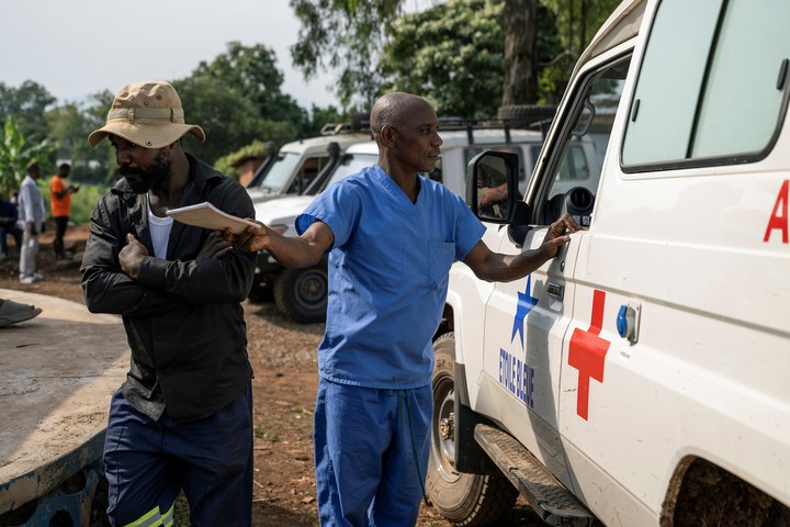 Emile Yombe, vestido de azul, voluntario de la Cruz Roja, junto a un conductor de ambulancia frente al Hospital General de Nyankunde, mientras esperan los resultados de las pruebas del señor Okito. Fotos de Arlette Bashizi para The New York Times.